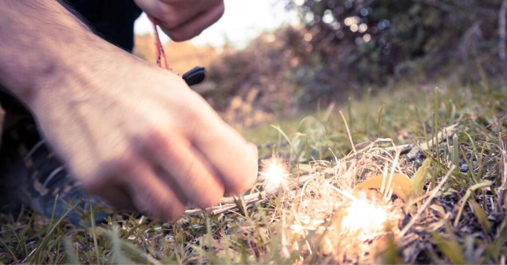 man's right hand lighting a fire on a grassy patch