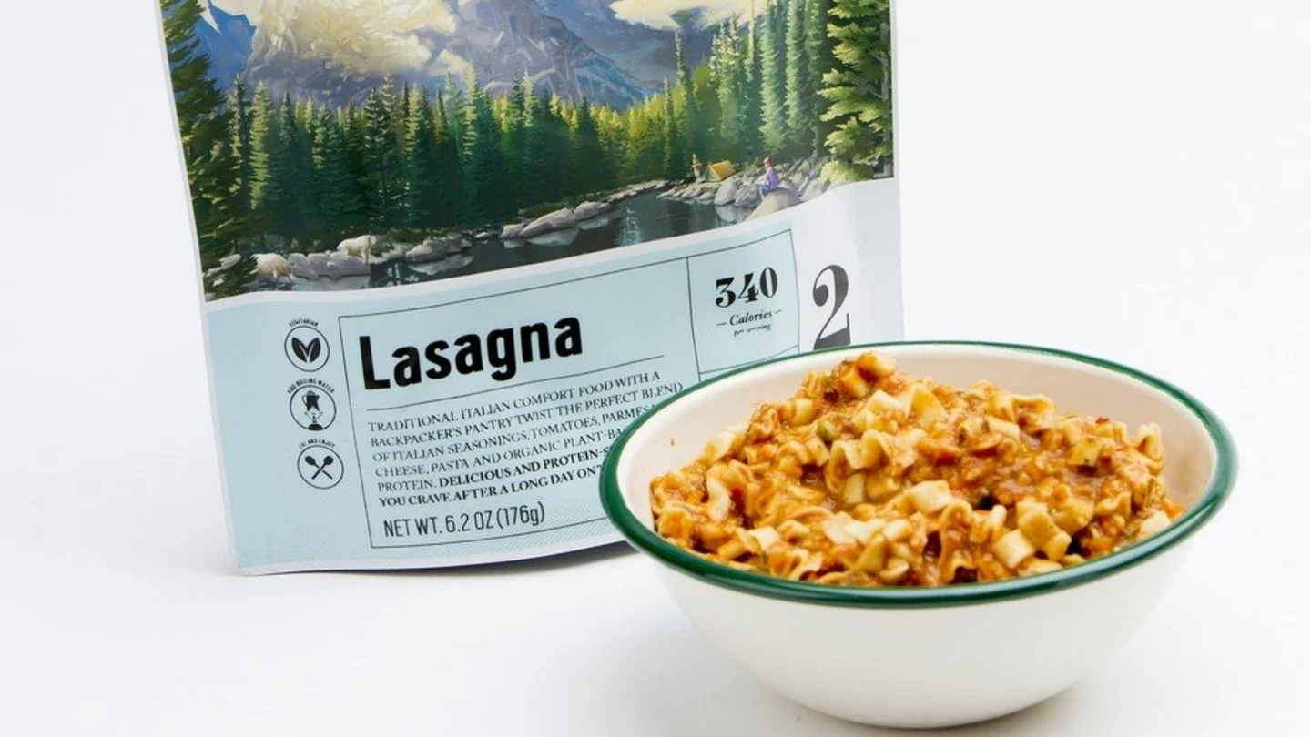 A tasty freeze-dried lasagna in a bowl beside an opened plastic pack. 