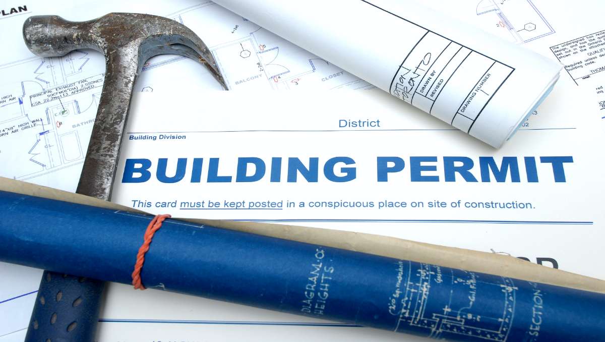 A blueprint and hammer on top of a building permit document.