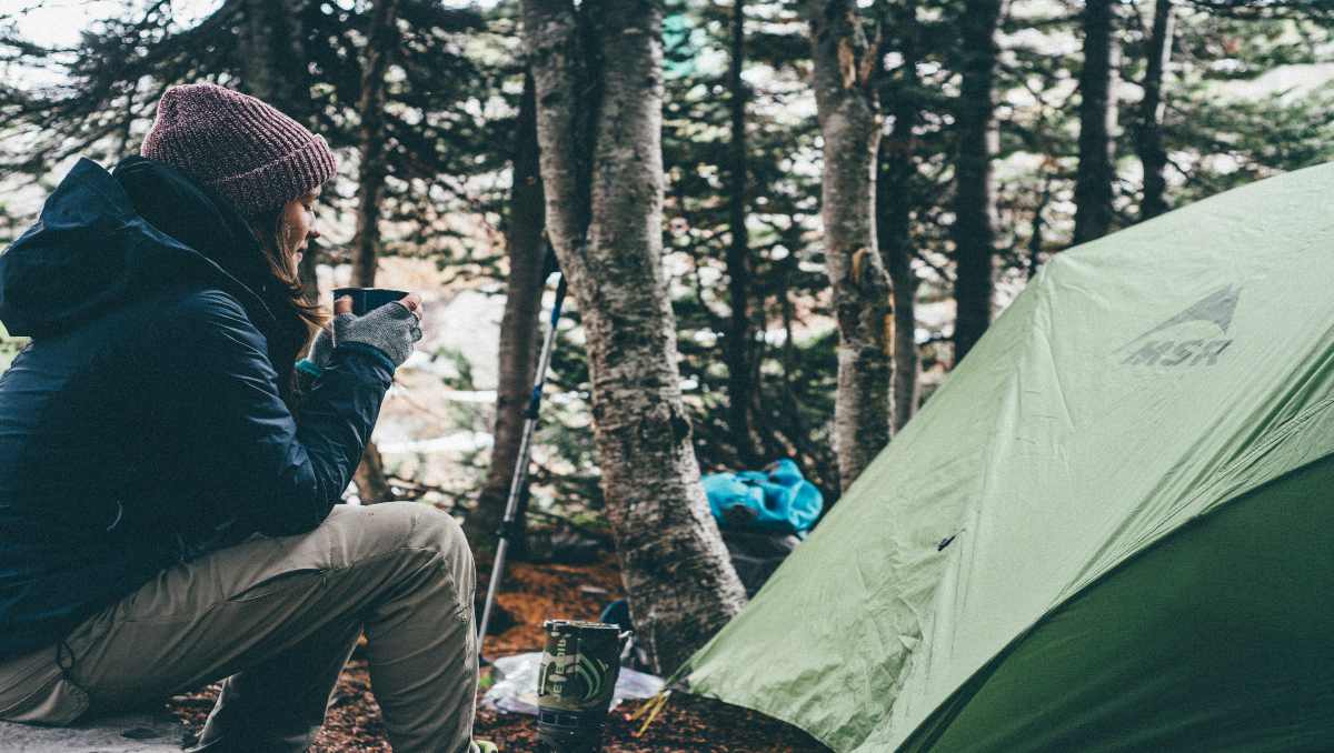 A female camper enjoying a drink outside her tent.
